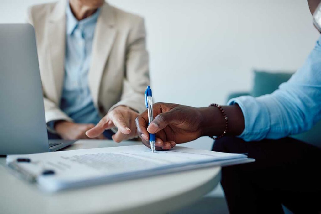 A couple reviews an insurance policy beside a home inventory, jewelry appraisal, and calculator.